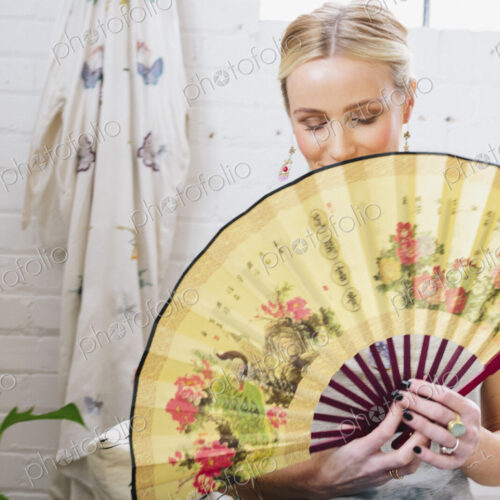 A woman holding an open Oriental fan hiding her face.