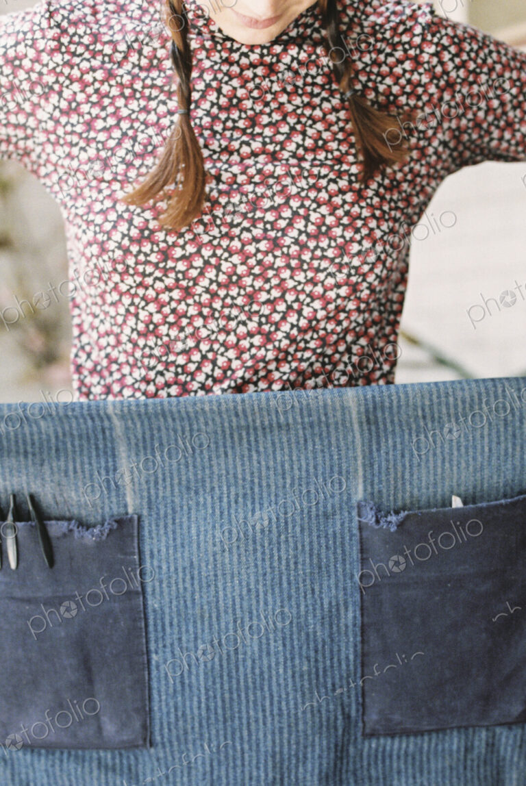 A woman holding and wrapping a denim apron aroud her waist.
