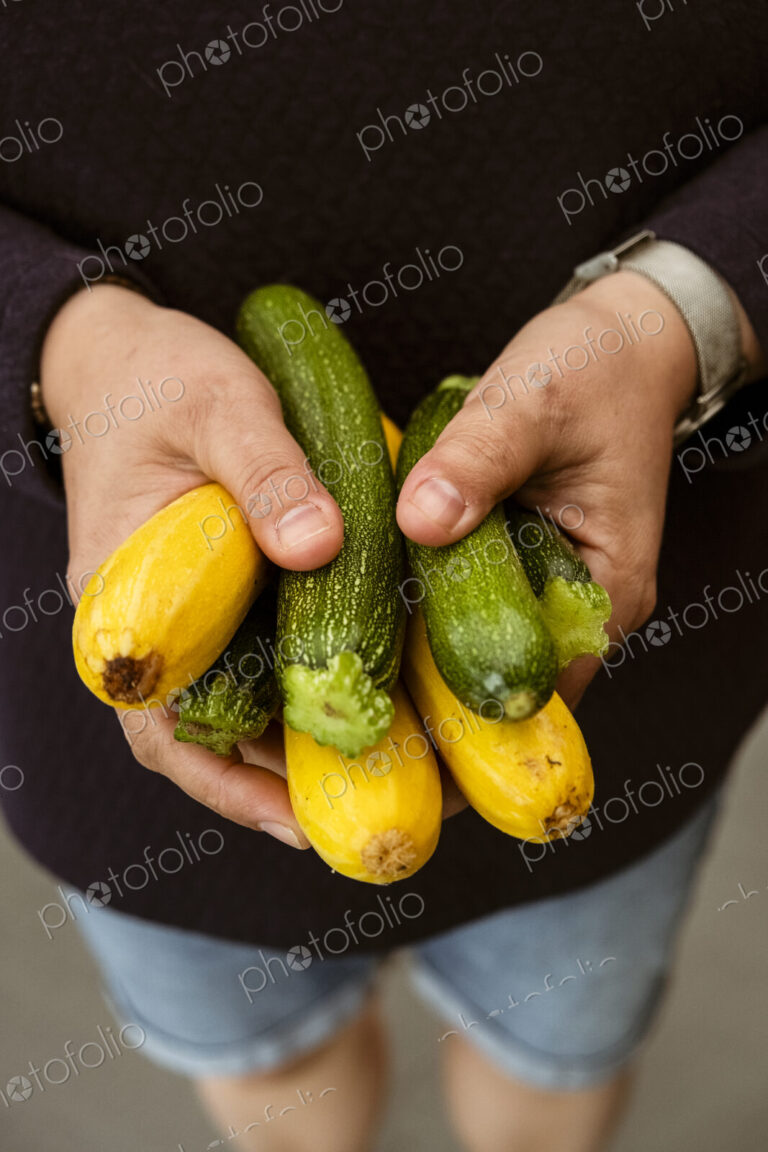 A woman holding out her hands holding a bunch of freshly picked yellow and green…