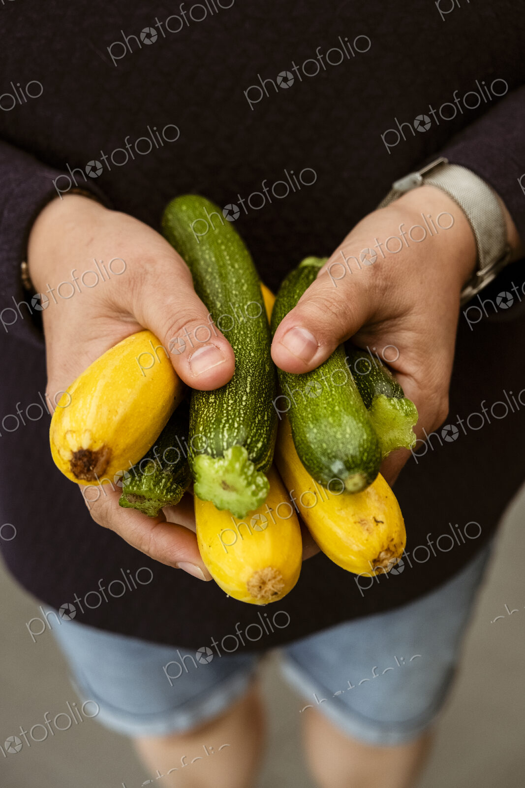 A woman holding out her hands holding a bunch of freshly picked yellow and green…