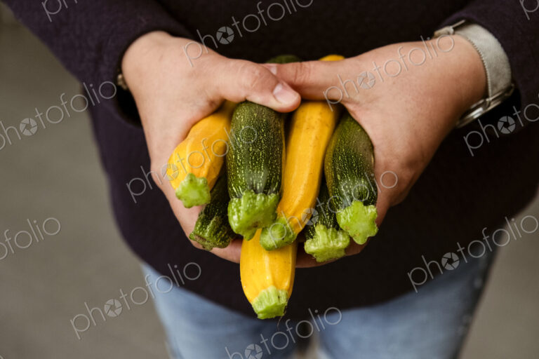 A woman holding out her hands holding a bunch of freshly picked yellow and green…