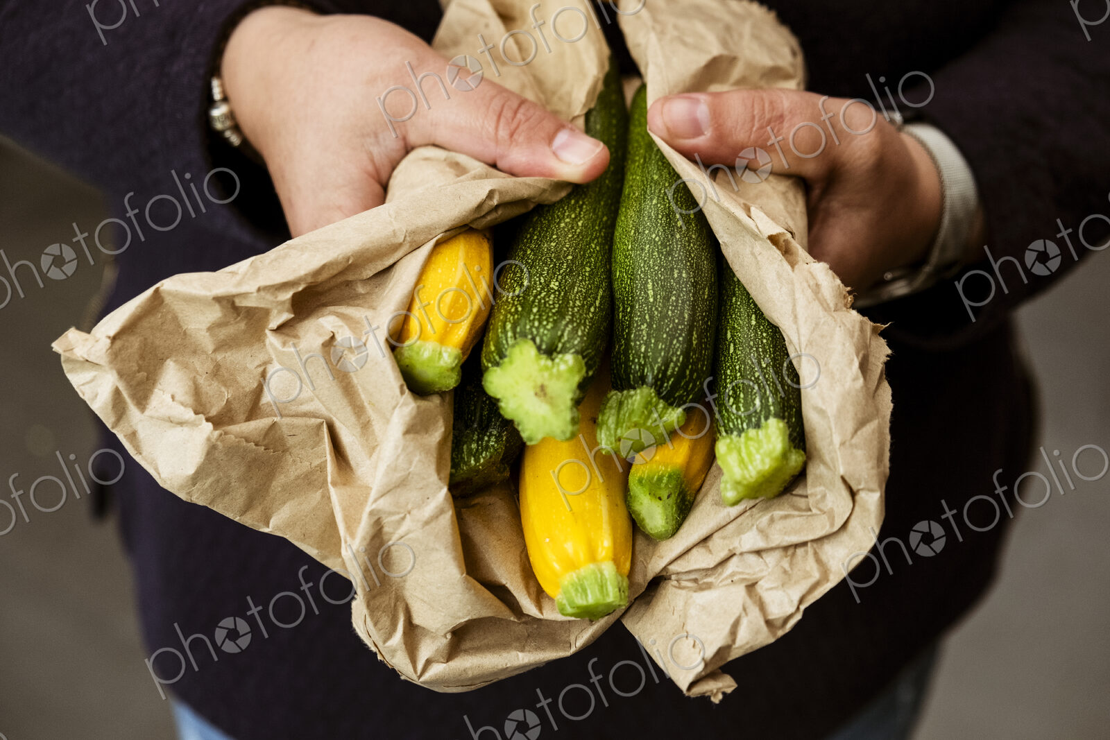 A woman holding out her hands holding a bunch of freshly picked yellow and green…