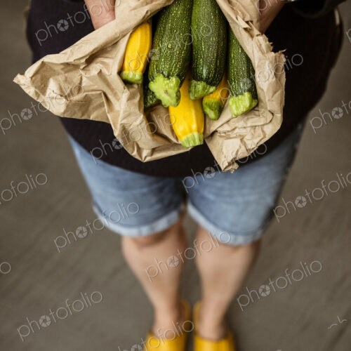 A woman holding out her hands holding a bunch of freshly picked yellow and green…