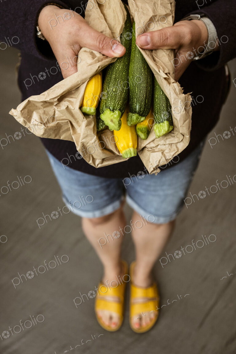 A woman holding out her hands holding a bunch of freshly picked yellow and green…