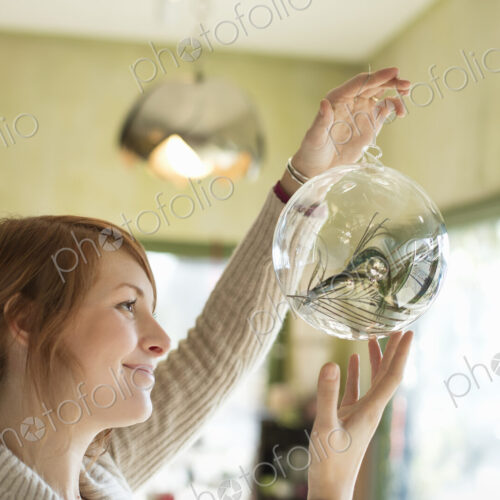 A woman holding up a large glass sphere, clear glass with a decorative objects inside.