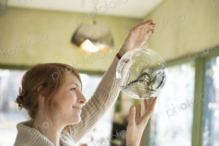 A woman holding up a large glass sphere, clear glass with a decorative objects inside.