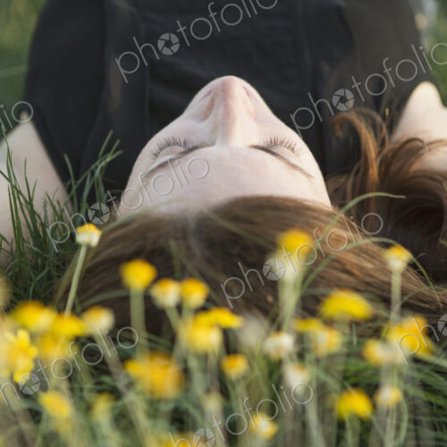 A woman in a black vest top and jeans lying on the grass with her hands behind her head. A woman in a black vest top and jeans lying on the grass with her hands behind her head.