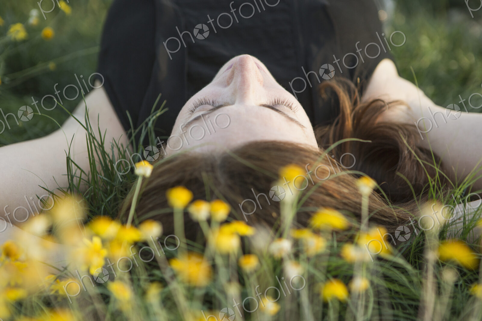 A woman in a black vest top and jeans lying on the grass with her hands behind her head.