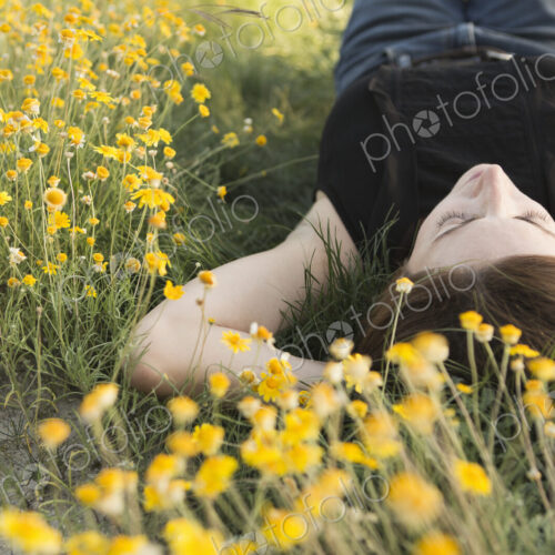 A woman in a black vest top and jeans lying on the grass with her hands behind her head. A woman in a black vest top and jeans lying on the grass with her hands behind her head.