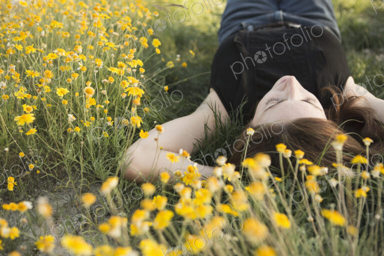 A woman in a black vest top and jeans lying on the grass with her hands behind her head.