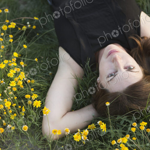 A woman in a black vest top and jeans lying on the grass with her hands behind her head. A woman in a black vest top and jeans lying on the grass with her hands behind her head.