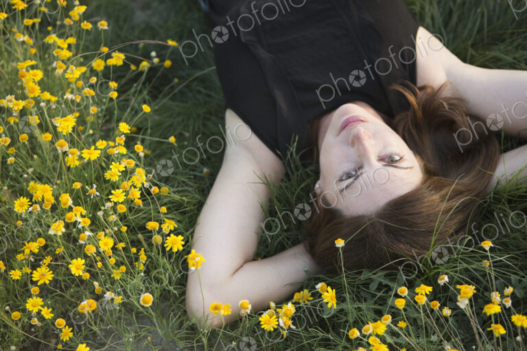 A woman in a black vest top and jeans lying on the grass with her hands behind her head.