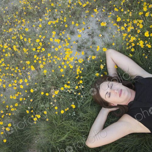 A woman in a black vest top and jeans lying on the grass with her hands behind her head. A woman in a black vest top and jeans lying on the grass with her hands behind her head.