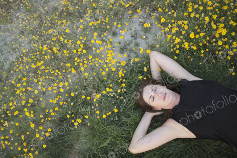 A woman in a black vest top and jeans lying on the grass with her hands behind her head.
