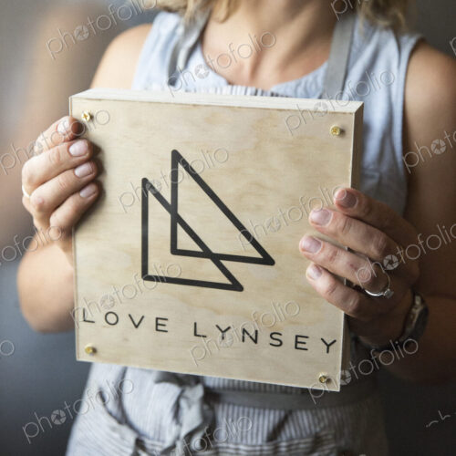 A woman in a blue apron holding her business sign, a square piece of wood with a… A woman in a blue apron holding her business sign, a square piece of wood with a…