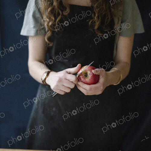 A woman in a blue apron peeling an apple with a knife.