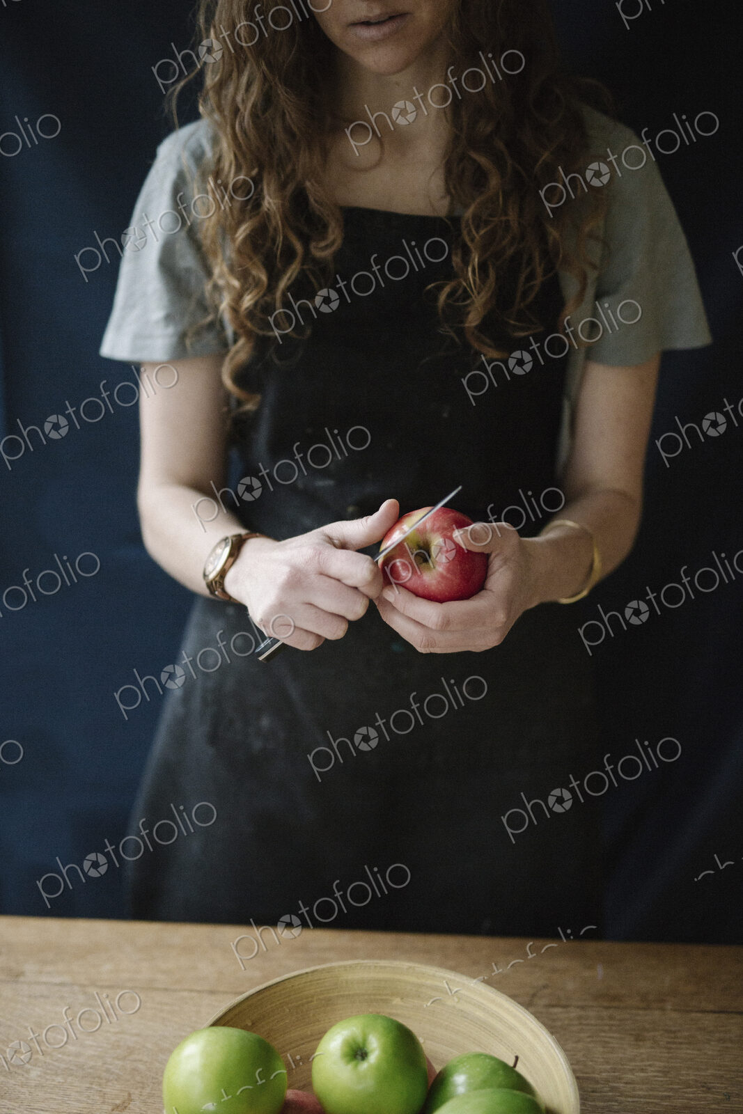 A woman in a blue apron peeling an apple with a knife.
