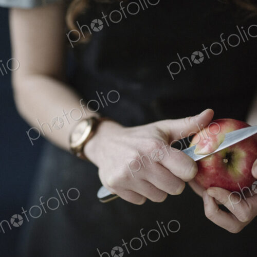 A woman in a blue apron peeling an apple with a knife.