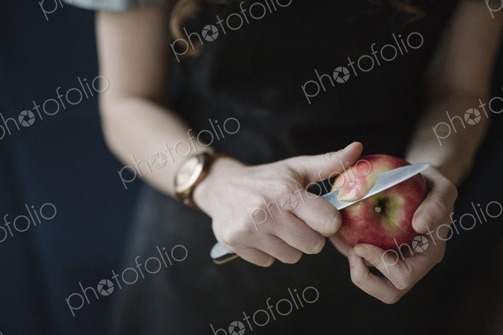 A woman in a blue apron peeling an apple with a knife.