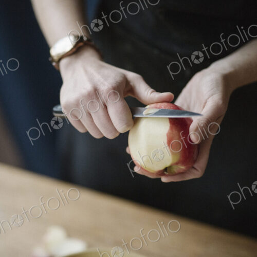 A woman in a blue apron peeling an apple with a knife. A woman in a blue apron peeling an apple with a knife.