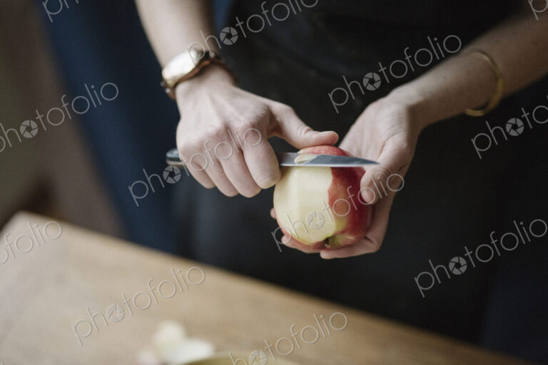 A woman in a blue apron peeling an apple with a knife.