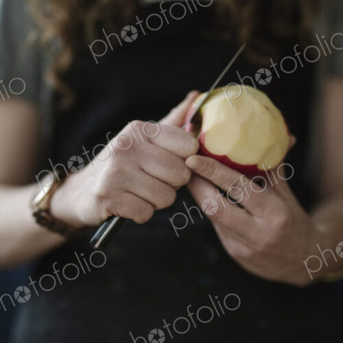 A woman in a blue apron peeling an apple with a knife. A woman in a blue apron peeling an apple with a knife.