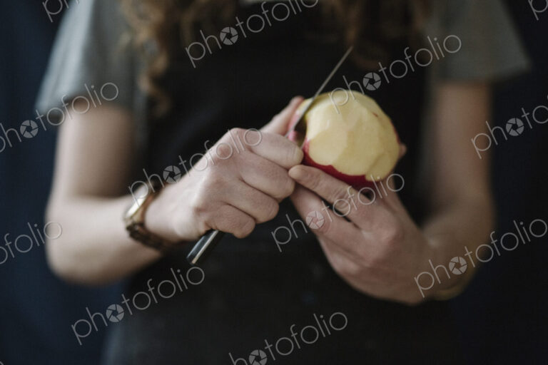 A woman in a blue apron peeling an apple with a knife.