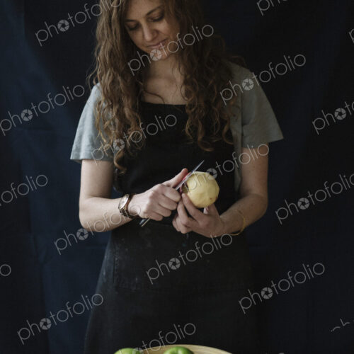 A woman in a blue apron peeling an apple with a knife.