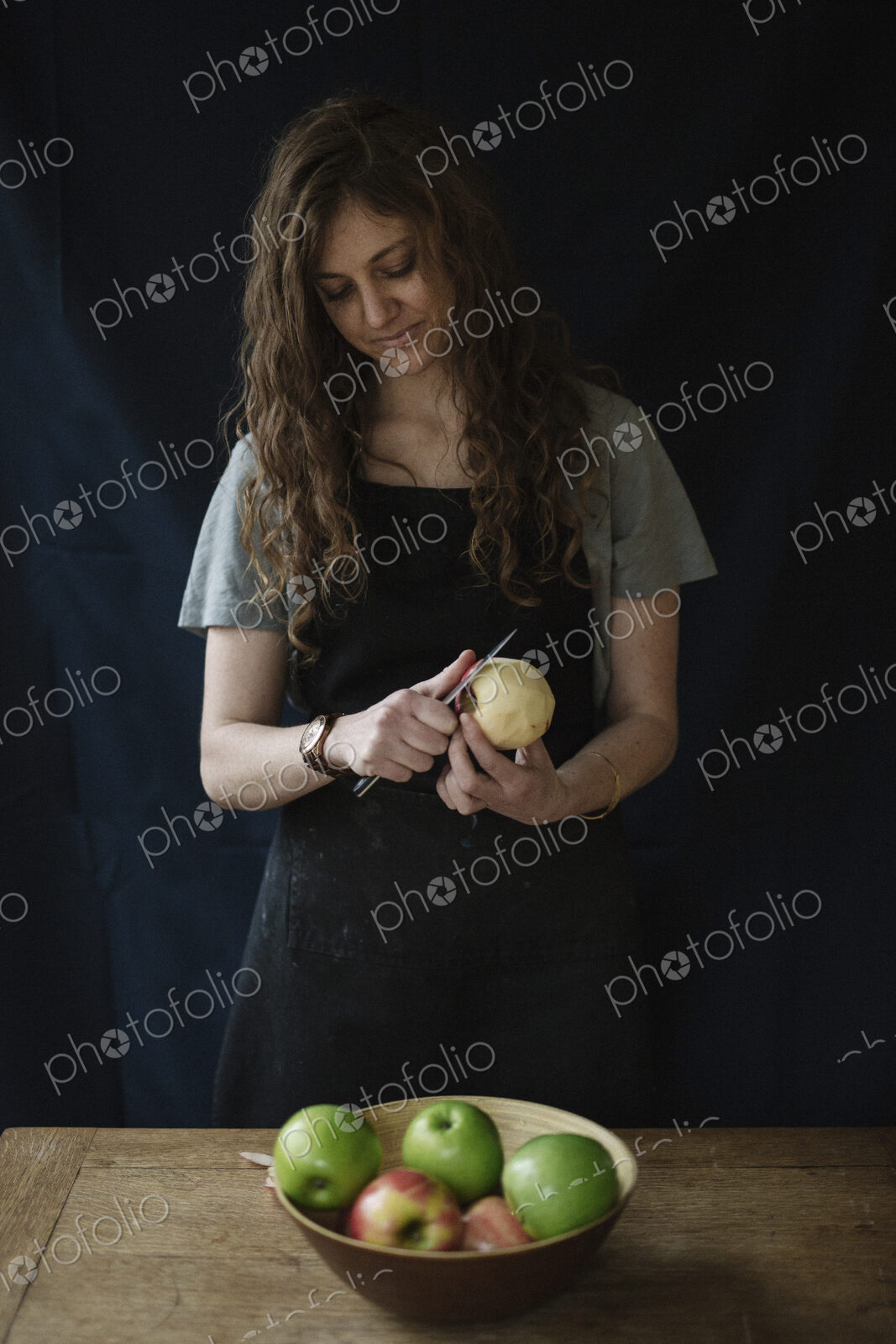 A woman in a blue apron peeling an apple with a knife.