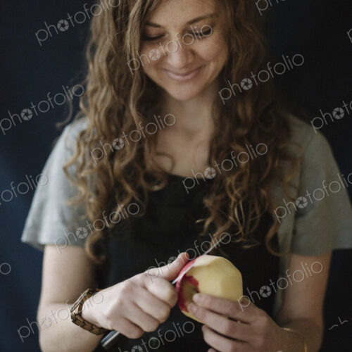 A woman in a blue apron peeling an apple with a knife. A woman in a blue apron peeling an apple with a knife.