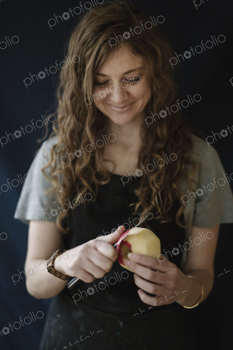 A woman in a blue apron peeling an apple with a knife.