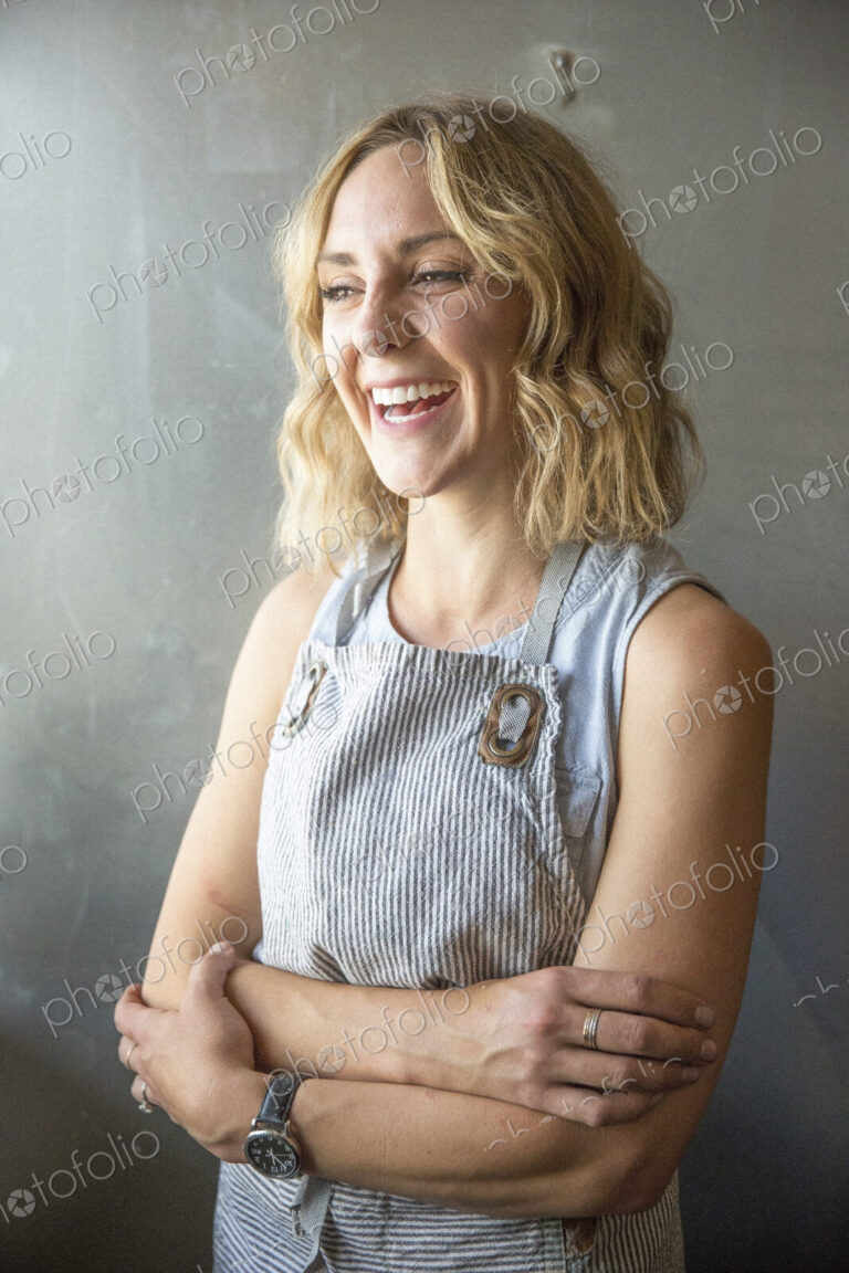 A woman in a blue work apron with arms folded, smiling.