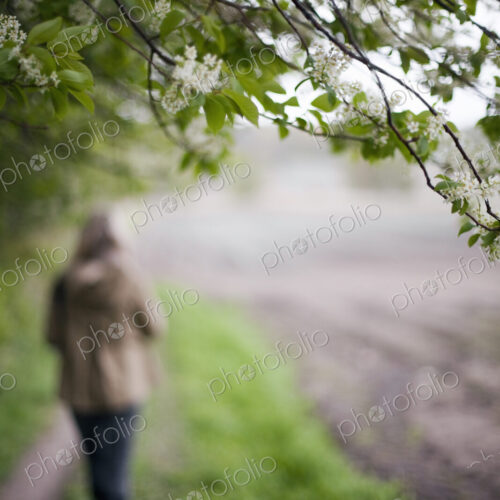 A woman in a brown hooded coat and hat walking along a path beside a ploughed field. A woman in a brown hooded coat and hat walking along a path beside a ploughed field.