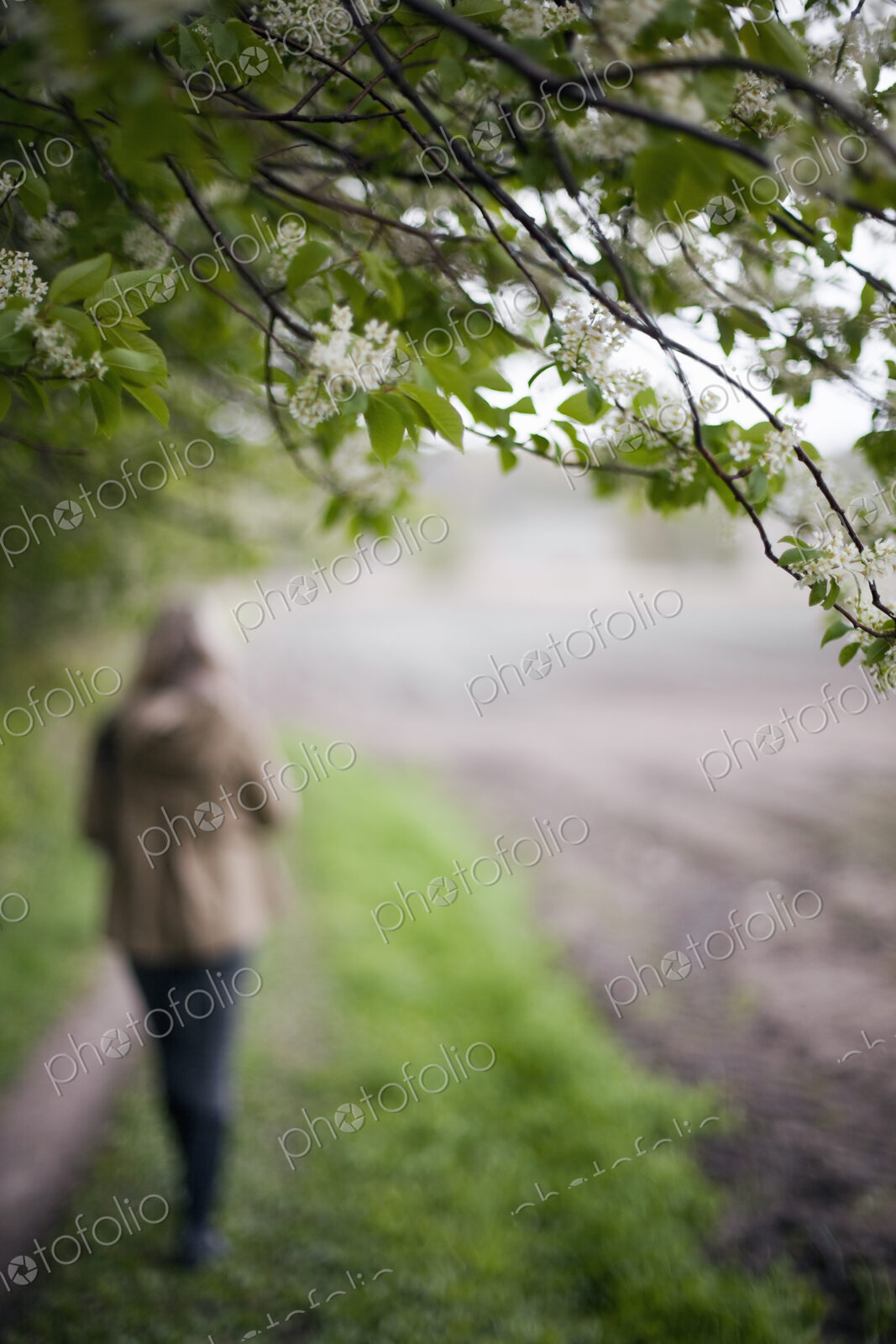 A woman in a brown hooded coat and hat walking along a path beside a ploughed field.