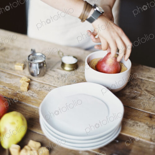 A woman in a domestic kitchen cooking. Dipping fresh organic pears into a sauce for… A woman in a domestic kitchen cooking. Dipping fresh organic pears into a sauce for…