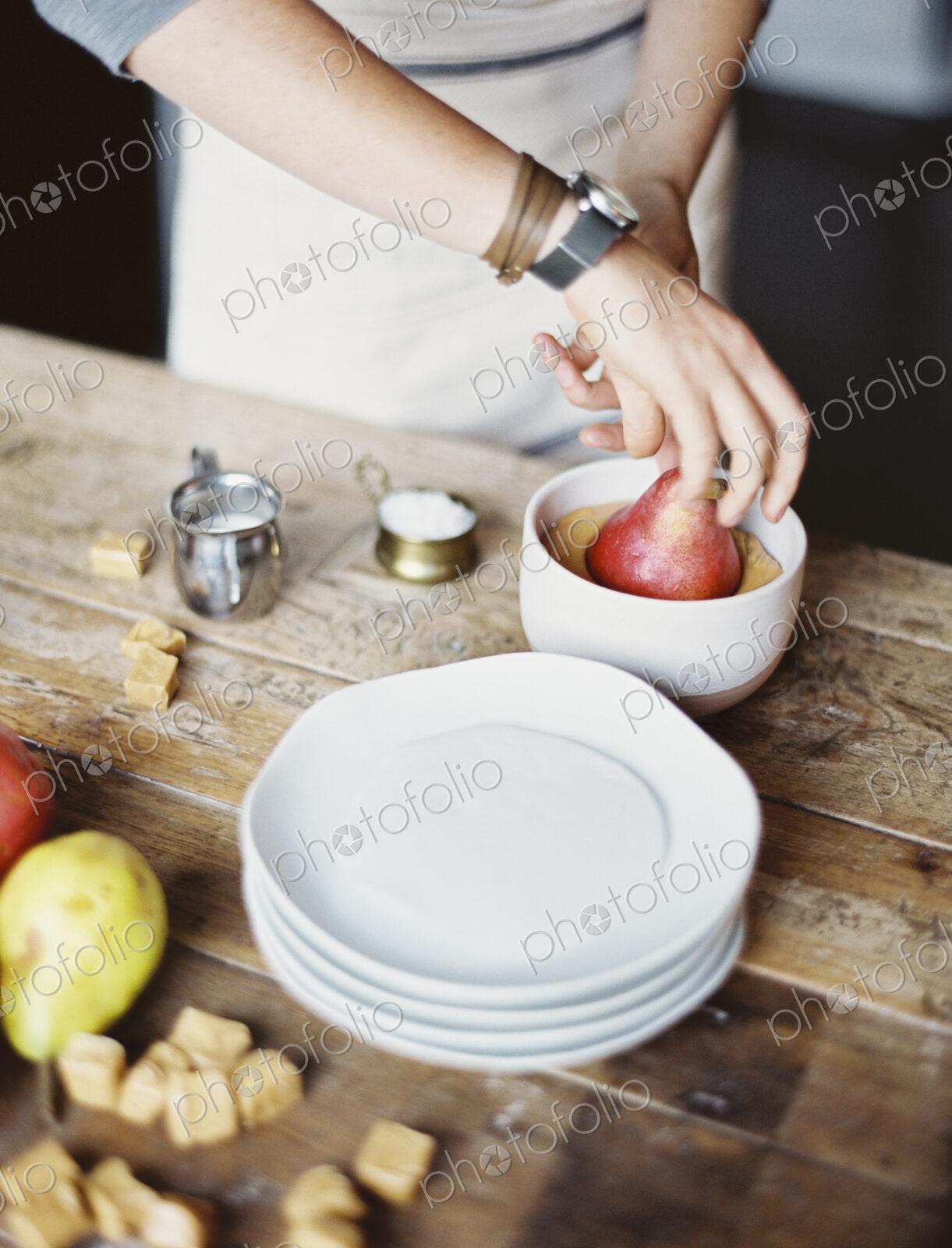 A woman in a domestic kitchen cooking. Dipping fresh organic pears into a sauce for…