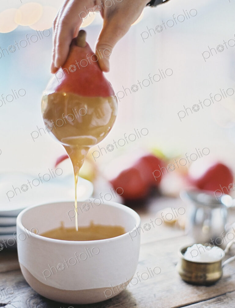 A woman in a domestic kitchen cooking. Dipping fresh organic pears into a sauce for…