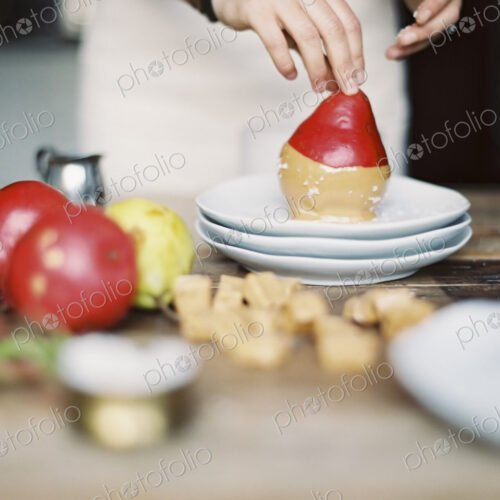 A woman in a domestic kitchen cooking. Dipping fresh organic pears into a sauce for… A woman in a domestic kitchen cooking. Dipping fresh organic pears into a sauce for…