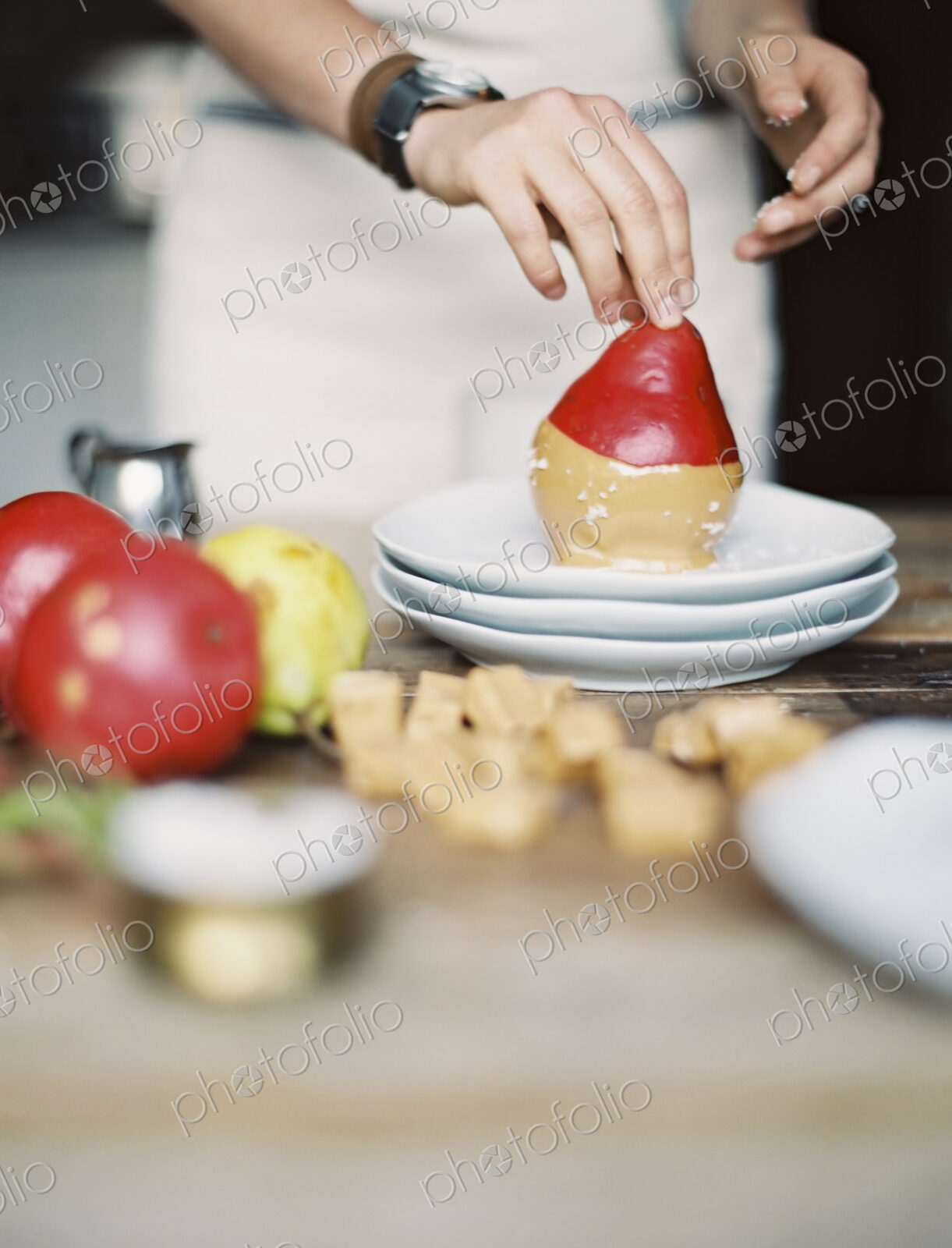 A woman in a domestic kitchen cooking. Dipping fresh organic pears into a sauce for…