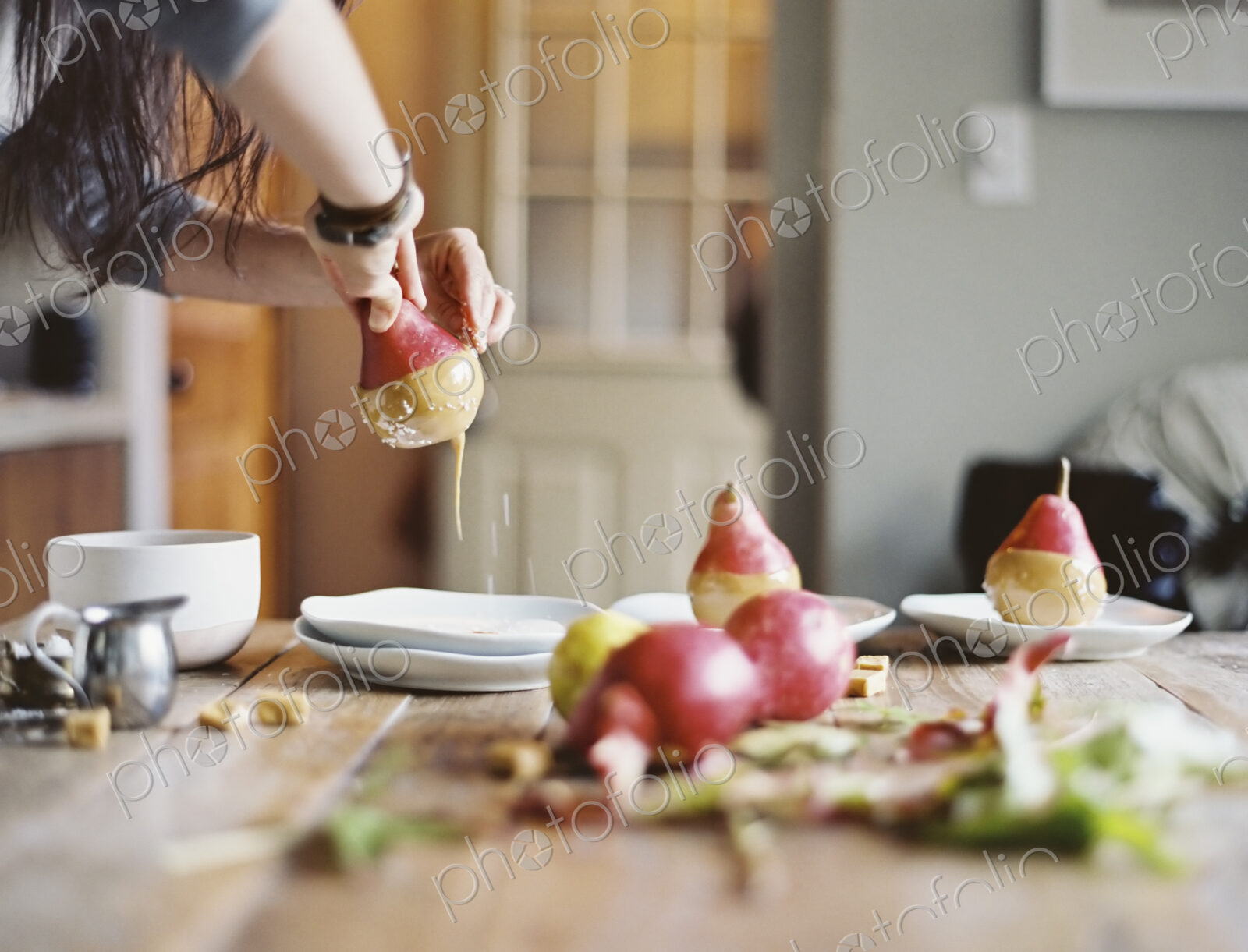 A woman in a domestic kitchen cooking. Dipping fresh organic pears into a sauce for…