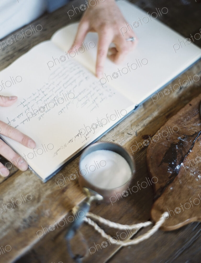 A woman in a domestic kitchen, reading a recipe book.