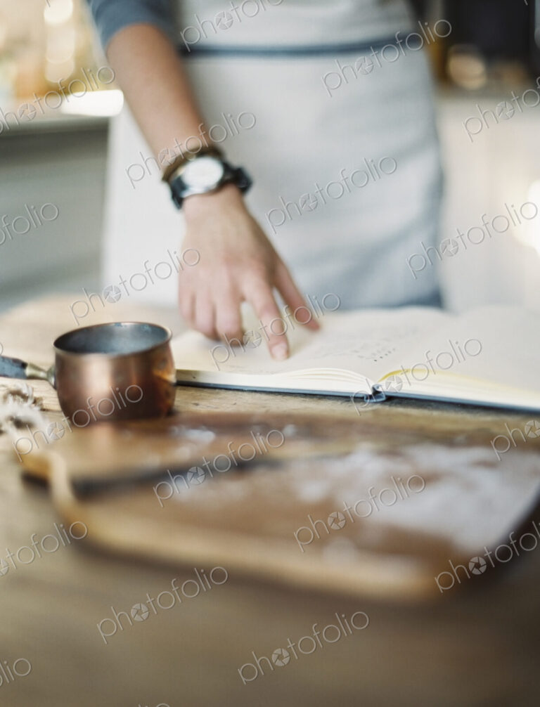 A woman in a domestic kitchen, reading a recipe book.