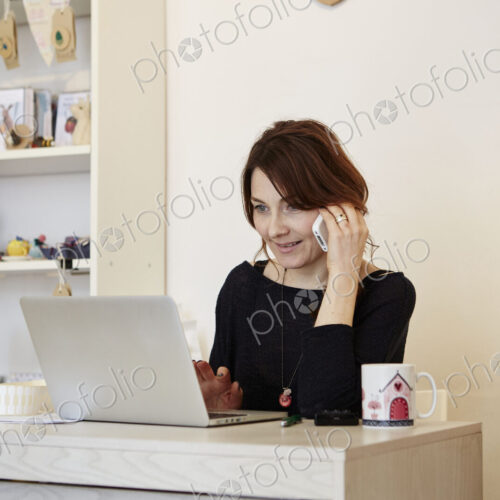 A woman in a gift shop using a laptop, making a call.
