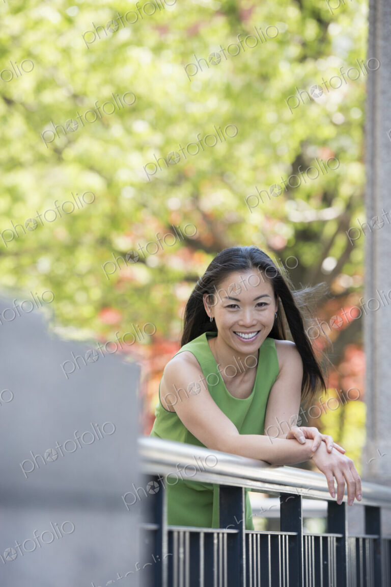 A woman in a green dress outdoors in a city park under trees in blossom.