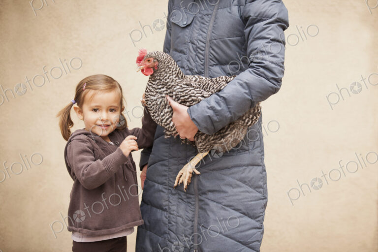 A woman in a grey coat holding a black and white chicken with a red coxcomb under one…