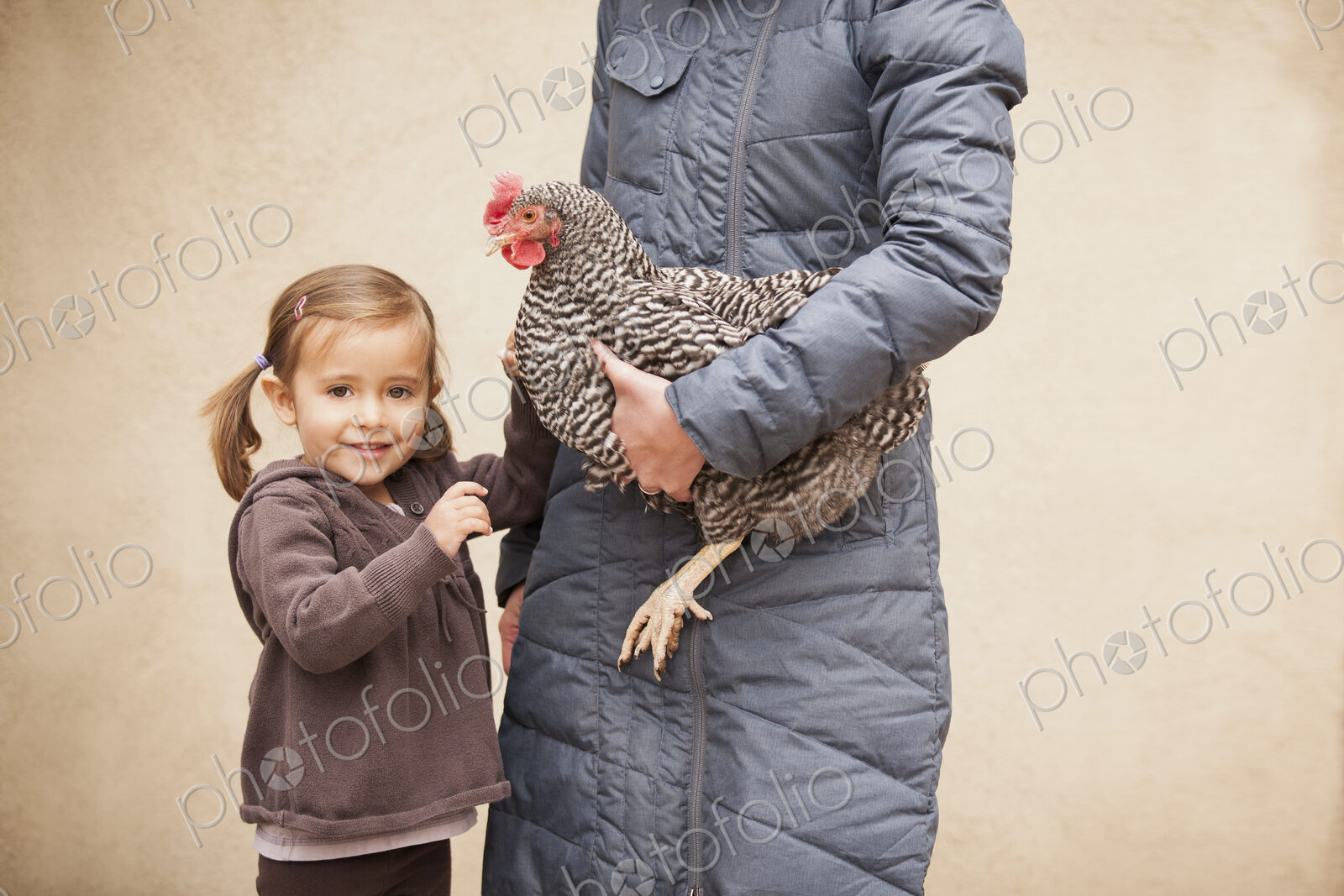 A woman in a grey coat holding a black and white chicken with a red coxcomb under one…