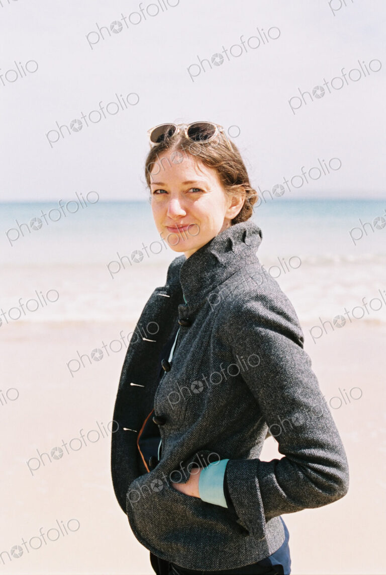A woman in a grey coat on the beach.