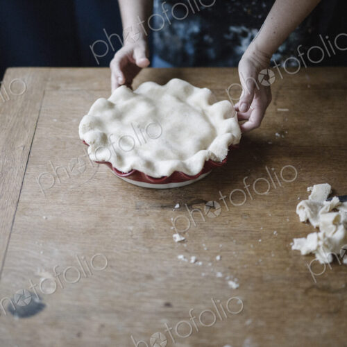 A woman in a kitchen decorating the pastry top of a home made pie. A woman in a kitchen decorating the pastry top of a home made pie.