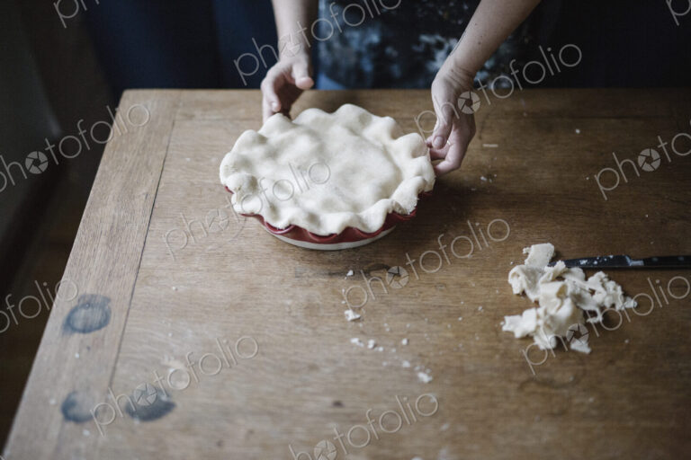 A woman in a kitchen decorating the pastry top of a home made pie.