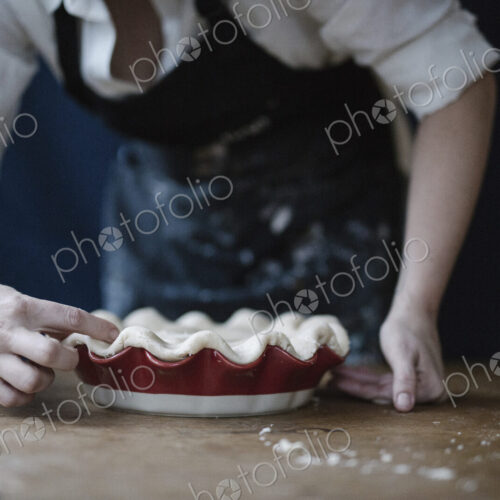 A woman in a kitchen decorating the pastry top of a home made pie. A woman in a kitchen decorating the pastry top of a home made pie.